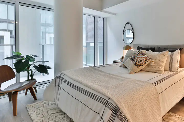 Kunstpflanze in einem Hotelzimmer. Bett mit beiger Bettdecke. Große Fenster die die Kunstpflanze für Hotelzimmer gut zur geltung kommen lässt. Aplanta.